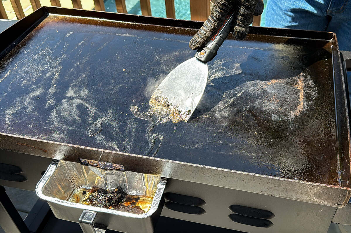a metal scraper running across debris on a Blackstone griddle