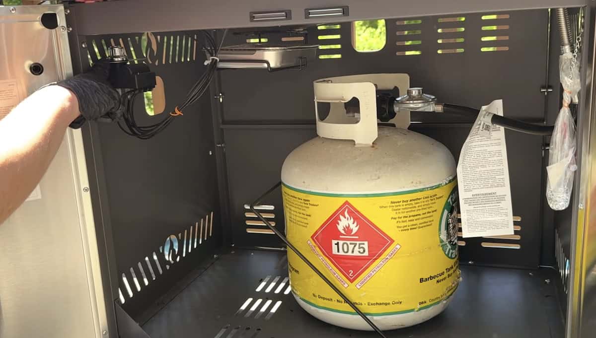 Propane tank inside an outdoor kitchen setup, ready for grilling.