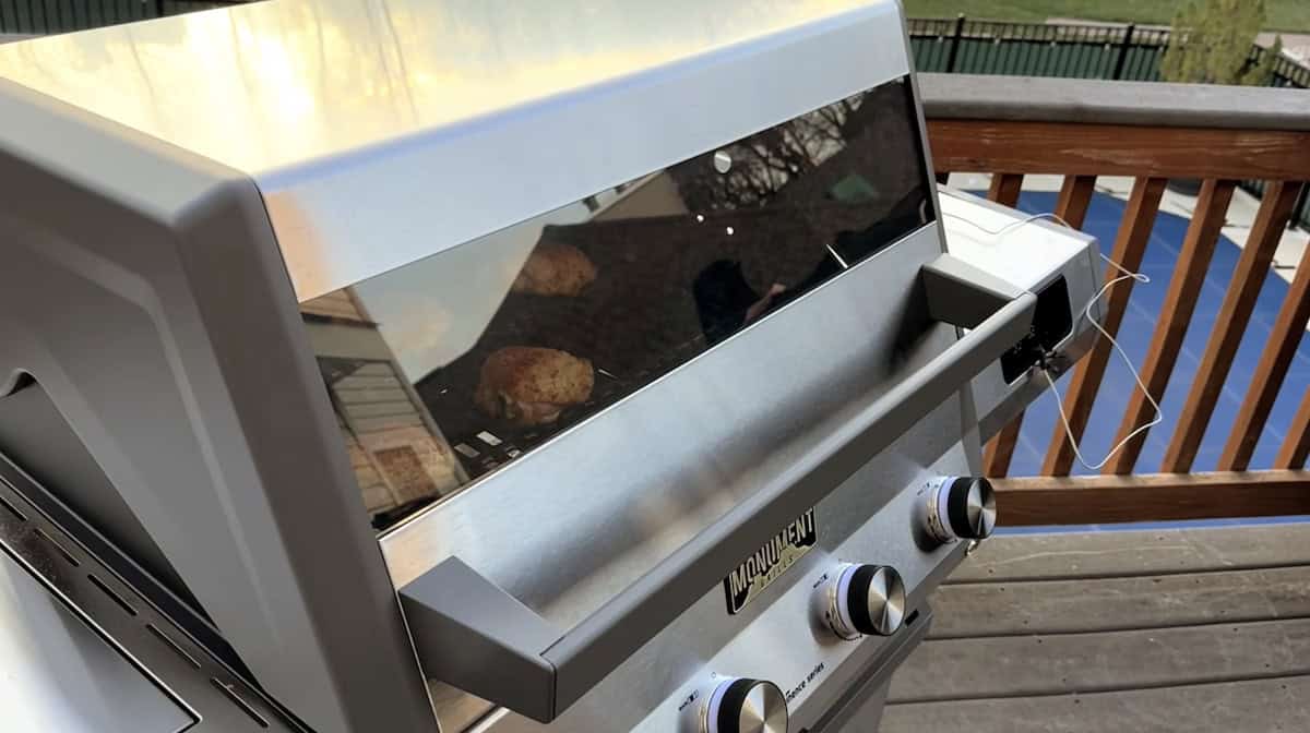 Outdoor gas grill with glass lid and control knobs for grilling.
