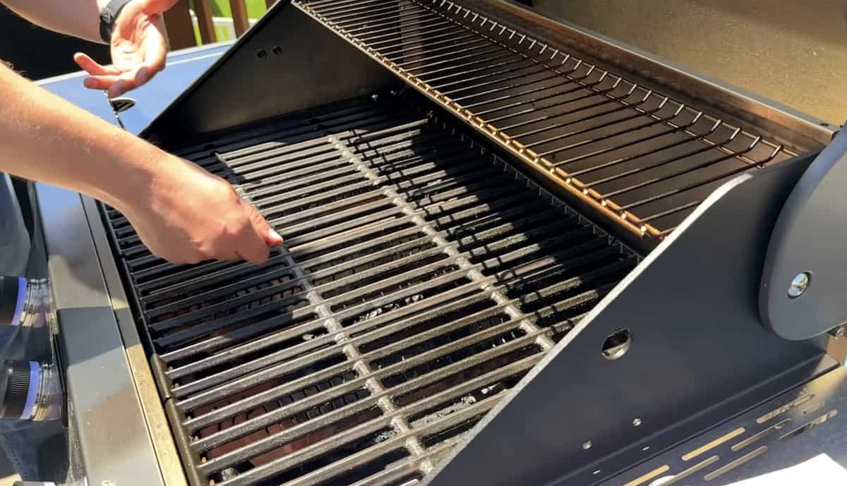 Close-up of a person cleaning a barbecue grill with a wire brush.